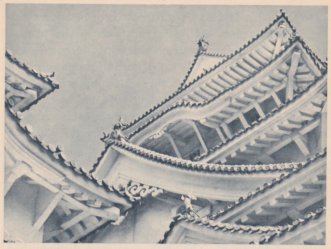 Black-and-white photograph, taken from below, of the undersides of several overlapping tiled roofs against a pale sky, their curved edges lined with small round tile ends. Timber brackets and slanting beams show under the eaves, a scrolled carved ornament hangs under a curved gable at the center left, and a small pointed ornament stands on a ridge near the top center. A separate roof corner shows at the upper left.