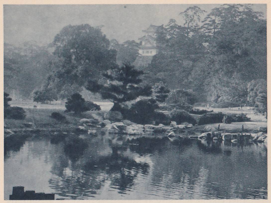Black-and-white photograph in haze across a pond whose far edge is lined with rocks, toward a hill thick with trees, among them pines of several shapes. A single small white-walled building with a pale roof shows high among the trees at the upper center. Reflections fill the pond, and a few dark squared posts stand at the lower left corner.