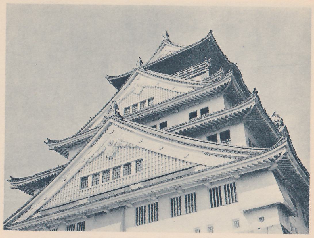 Black-and-white photograph, taken from below, of the upper parts of a building of stacked tiled roofs against the sky: large pale gables with lattice-patterned panels and rows of small windows, curved eaves with round tile ends, ornaments at the ridge ends, and below them white walls with barred windows. A railing shows high up at the top center.