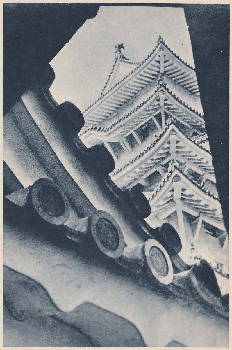 Black-and-white photograph looking up through a gap framed by dark roof edges, where large round tile ends in a row run diagonally across the left side. Through the gap rises a building of several stacked tiled roofs with wide eaves and rows of exposed rafters and beams against a pale sky, with a small ornament on its top ridge. A smooth curved tile surface fills the lower left.