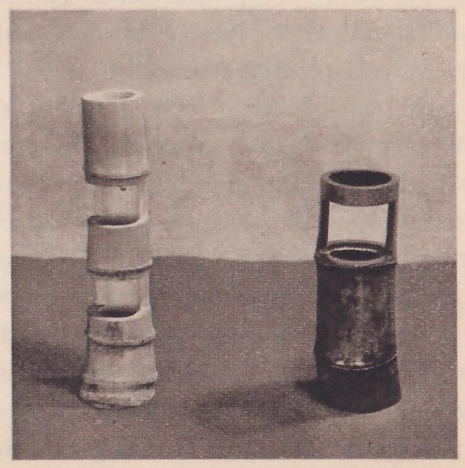 Photograph of two bamboo vases against a gray ground: at the left a pale tall one cut in three steps, and at the right a dark short one with a ring of bamboo held above its mouth by two uprights.