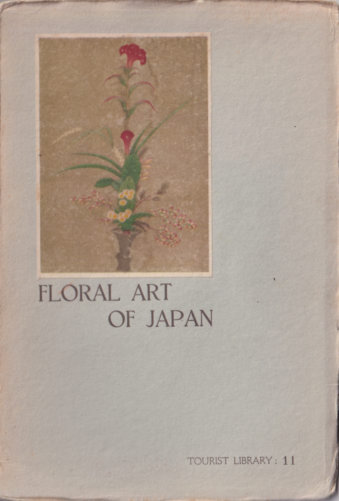 Front cover of the pale blue-gray paper wrapper: a colored picture pasted on it of an arrangement in a slim gray-brown vase against a tan ground: two red flowers on a tall stem, the upper one with a ruffled head, green leaves and grasses, and small yellow and pink flowers low down; below it the title Floral Art of Japan, and at the lower right Tourist Library: 11.