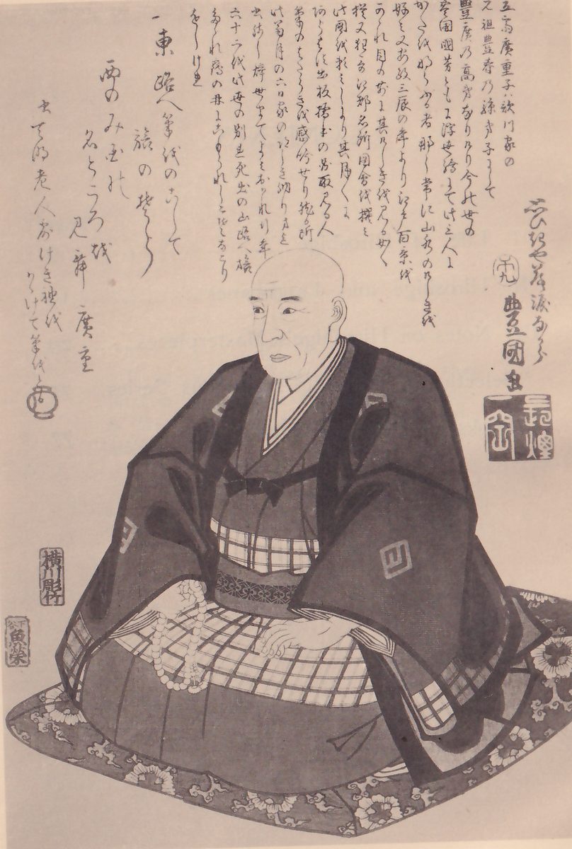 Print of a seated man with a bald head, his face turned toward the viewer's left. He wears a dark robe with square crests over a checked garment, and his hands rest in his lap with a string of beads across them. He sits on a cushion with a flower pattern. Writing fills the top: a eulogy in columns above his head, and down the left side his death poem, signed Hiroshige. At the upper right are the artist’s signature and a square seal, and two small seals stand at the lower left edge.