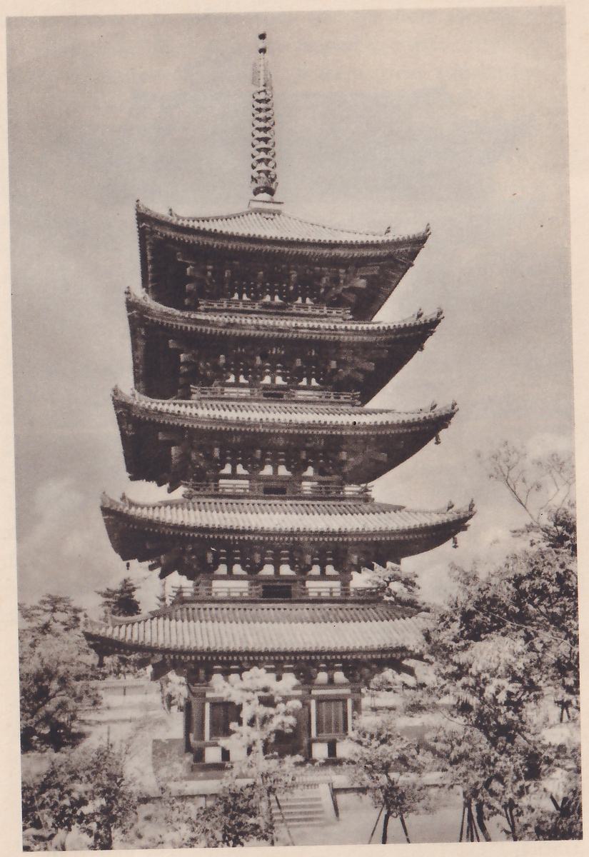 Photograph of a tall pagoda with five stacked tiled roofs, each smaller than the one below, topped by a thin spire made of rings, seen from below against a cloudy sky with leafy trees at the left and right and a few steps at its base.