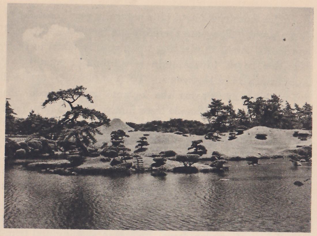 Photograph across a pond with rippled water to a far shore of low, grass-covered mounds with small clipped pines on them and a taller pine leaning at the left; a small cone-shaped hill shows behind the mounds and trees line the horizon under a cloudy sky.