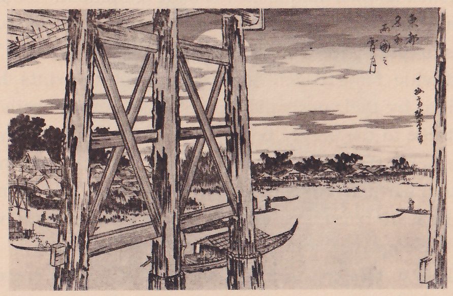 Black-and-white print of a wide river seen between the thick timber posts and crossbraces of a bridge, which fill the left half of the picture. Small boats lie on the water, two with a figure standing in them, and low roofs and trees line the far shore and the horizon. A pale disc shows at the top center behind the beams. A title column and a signature column of Japanese characters stand at the upper right.