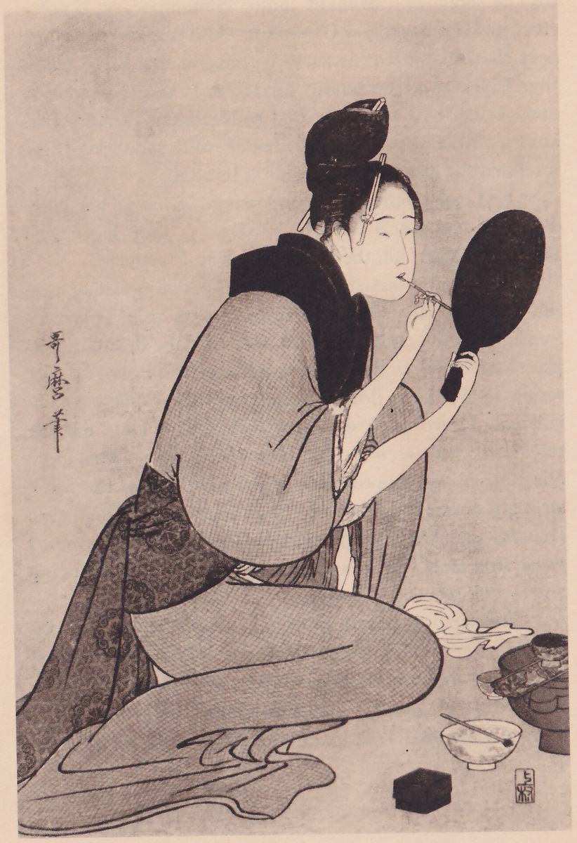Black-and-white print of a figure kneeling, bent forward, filling most of the picture, the hair in a high knot with pins, holding a round hand mirror in one hand and a thin stick at the lips with the other. The figure wears a wide dark collar, a loose robe and a dark patterned sash. On the floor at the lower right are a small tiered stand with bowls, a bowl with a stick laid across it, a small square box and a crumpled pale cloth. A signature column stands at the left and a seal at the lower right.