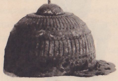 Black-and-white photograph of a dark dome with a small knob and a thin spike at its top, ribbed with many close vertical lines, and flaring at the lower edge into a thin brim at the right.