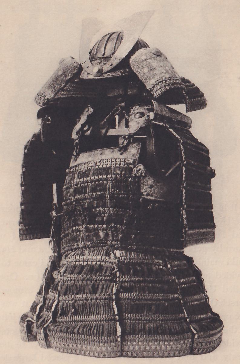 Black-and-white photograph of a suit of armour on a stand. A rounded helmet with a pale curved plate at its front sits at the top between two broad patterned flaps. Below them a dark body of closely laced horizontal rows has a small rounded fitting at its center right and a few cords across it. A skirt of laced bands, with pale vertical cords down it in several places, flares out toward the bottom.