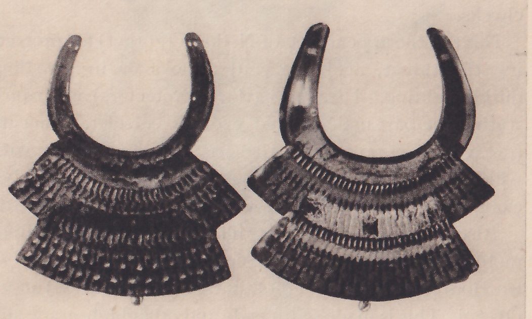 The lower of three black-and-white photographs on the page: a pair of objects side by side, each a horseshoe-shaped dark curve open at the top, above two wide fan-shaped tiers of laced bands. The tiers of the one at the right show pale patches and a small square mark.