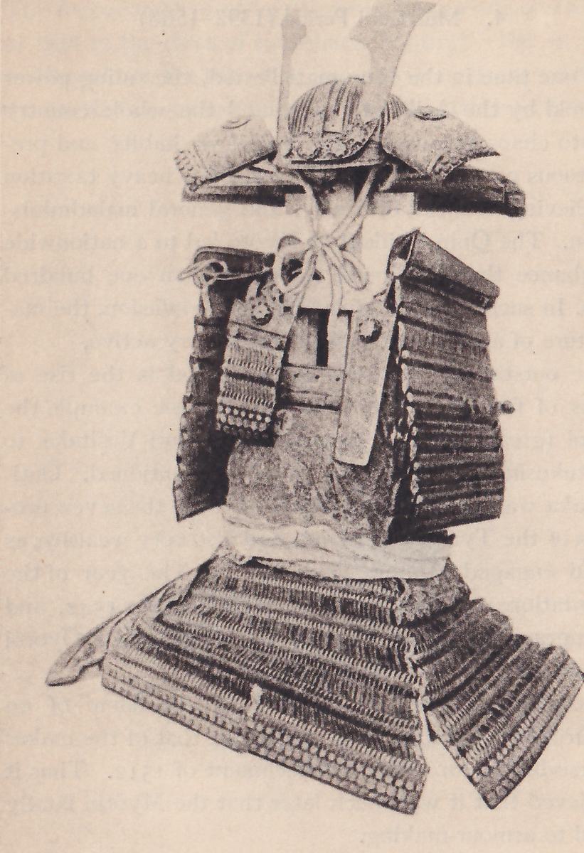 Black-and-white photograph of a suit of armour on a stand. A helmet with a ribbed bowl sits at the top on a flat dark board, with a thin pale plate rising behind it at the upper left and a pale cord knotted below it. Two rounded shoulder pieces spread to either side. Broad dark laced bands hang down both sides of a plain mottled panel at the center, a pale band crosses at the waist, and a wide skirt of laced bands flares out at the bottom.