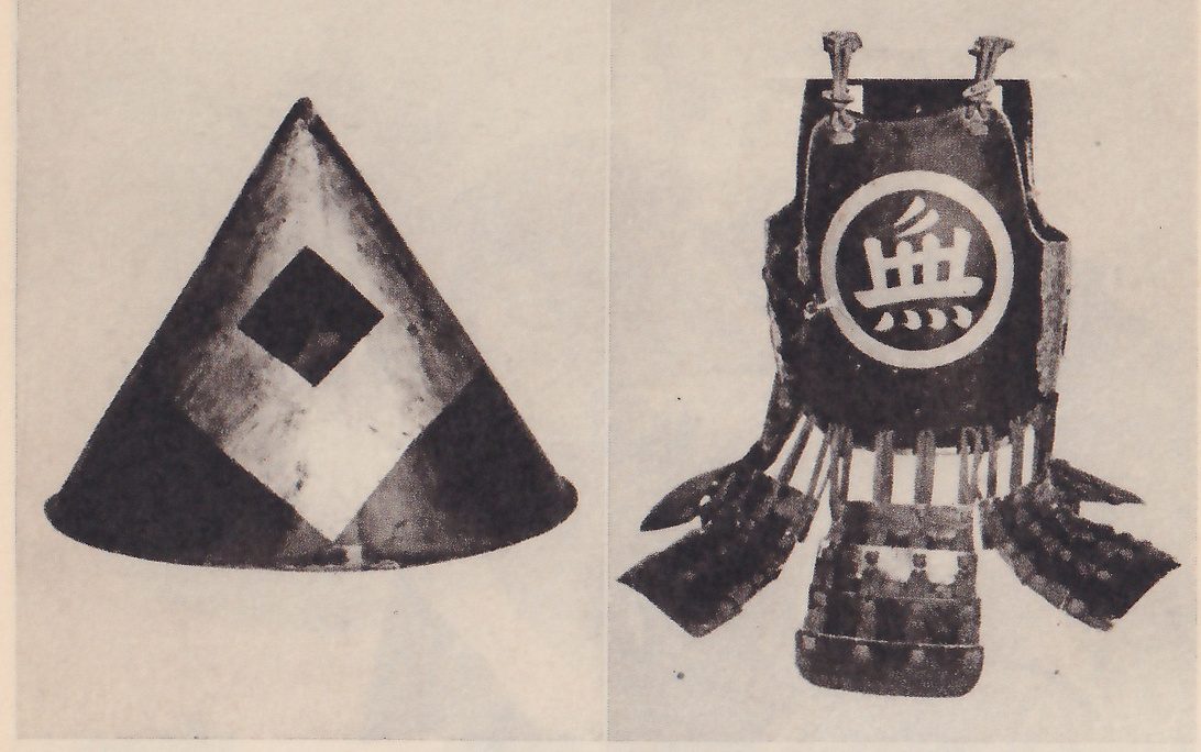 Two black-and-white photographs side by side. At the left, a plain cone-shaped hat with a large pale diamond on its side and a smaller dark diamond at the top of it. At the right, a dark upright body piece with two knotted cords at its top, the character 無 in a large white ring on its chest, pale vertical strips at its waist, and separate flaps and a short banded piece below.