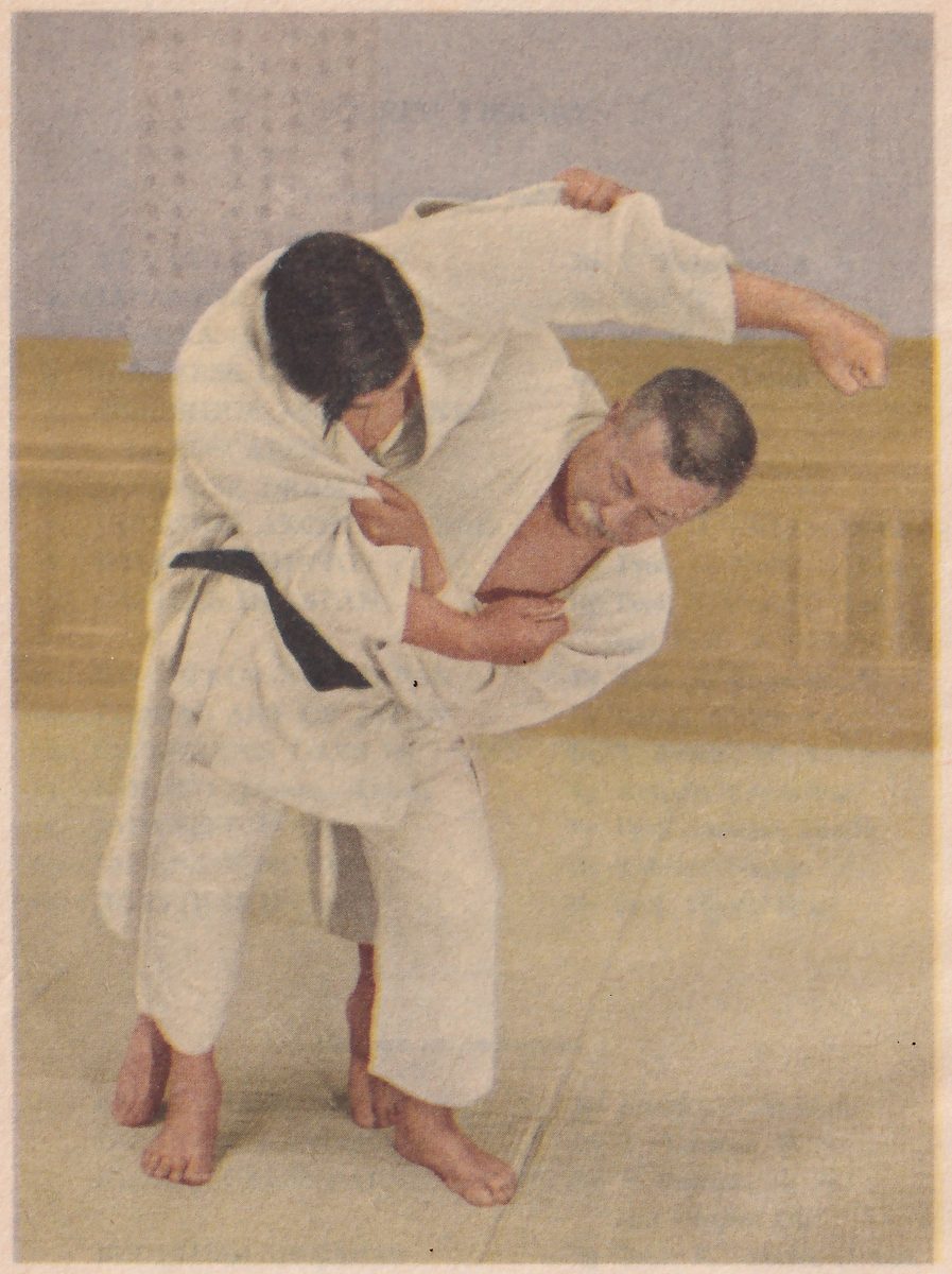 Color-tinted photograph of two men in white judo suits in the middle of a throw: the younger, dark-haired man in a black belt leans over the shoulder of the gray-haired man and grips his raised sleeve, while the gray-haired man, bent forward beneath him with his mouth open, holds the younger man's jacket at the chest with one hand and swings his other arm up and out; behind them a gray wall carries a vertical sheet of Japanese writing.