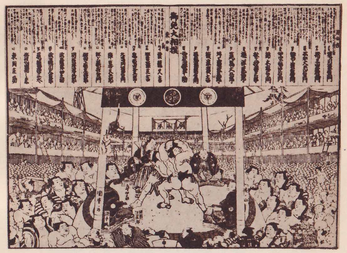 Black-and-white print of a crowded hall. A row of tall hanging strips written in vertical Japanese characters fills the top, with one wider strip at the center. Below, tiers of galleries filled with spectators run down both sides. A dark band carrying three round crests is held up by tall posts across the middle, and between the posts two men stand locked together in an open space, with another man bending beside them. Densely packed spectators fill the lower part, large in the foreground at the left and right.