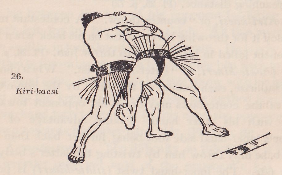 Line drawing of two wrestlers, each in a dark belt with an apron of hanging strands. The two men are tangled at the center, bent forward, with a dark belt and an apron of hanging strands at the upper center. One leg is lifted with the knee bent in the middle of the drawing and the other legs are planted apart at the bottom. A short line of dashes marks the ground at the lower right. Printed beside the drawing: 26. Kiri-kaesi