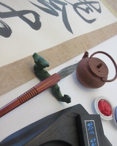 A brushed scroll with Master Takase's brush on its rest, an inkstone and ink stick, a small iron water pot and red seal paste